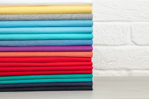 A stack of clean, neatly folded colored clothes on a light wooden table. Colors of rainbow. Place for text