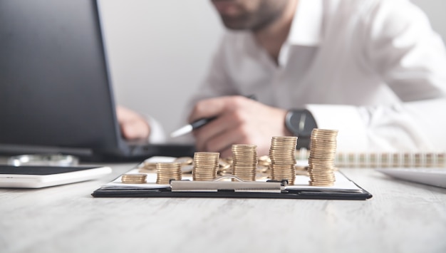 Stack of coins on the desk. Businessman working with laptop