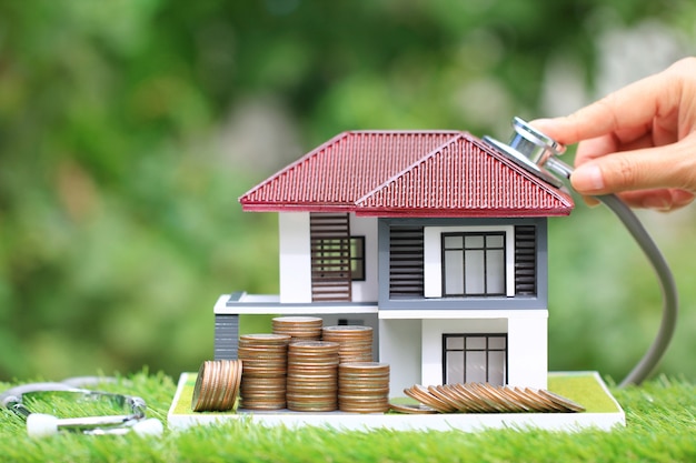 Stack of coins money and businesswoman using stethoscope to check model house