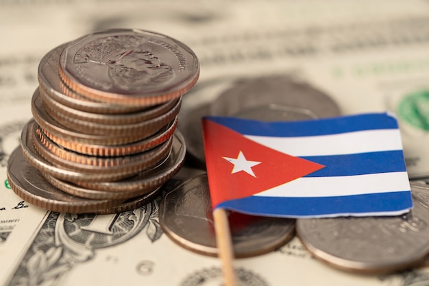 Stack of coins with Cuba flag on US dollar banknotes background.