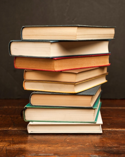 stack of colored vintage books on old wooden shelf with dark background