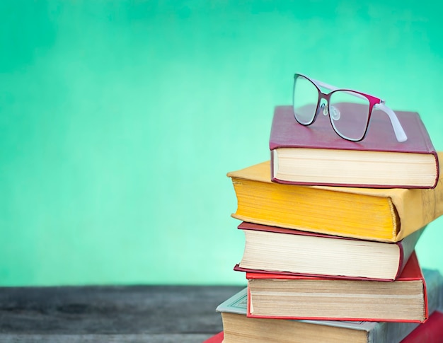 stack of colorful books and glasses close up on green and blue background