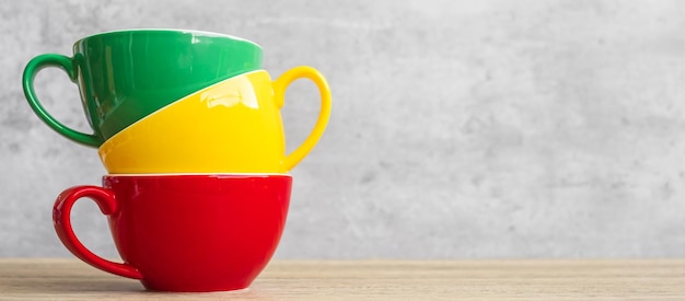 Stack of colorful coffee cups on wall background at cafe Green yellow and red color ceramic mug on table at home International coffee day concept