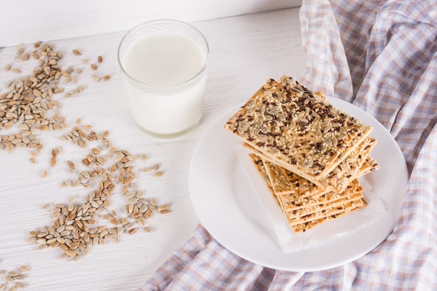 Stack of crispy wheat cakes with sesame flax and sunflower seeds on on a napkin on white wooden background  with glass of milk