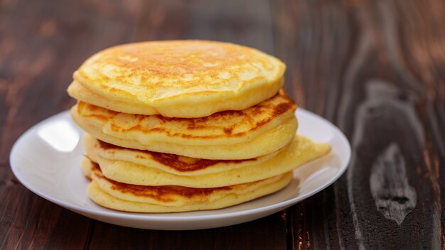 Stack of delicious pancakes in white plate on brown wooden background. It is a homemade breakfast Thick, soft, scented with butter.