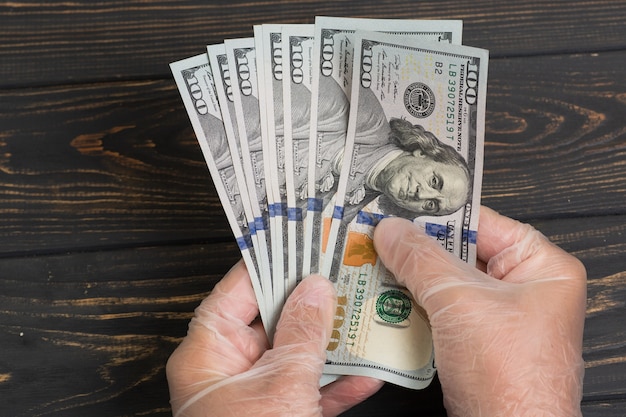 Stack of dollars USA in gloved hands on wooden table