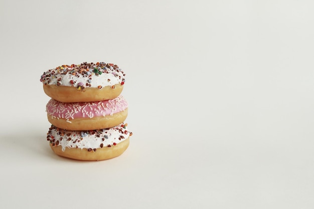 Stack of donuts in pink and white glaze with colored sprinkles on white background