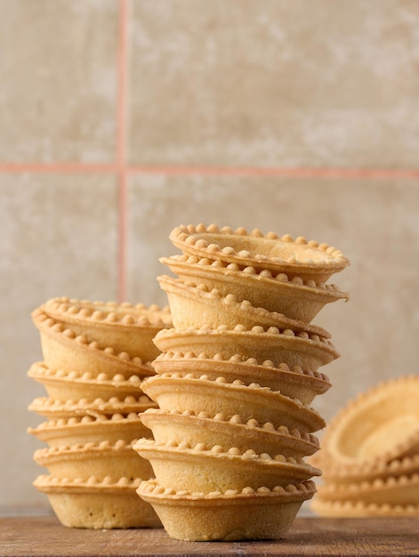 Stack of empty baked round canape baskets on a wooden board round empty tartlets