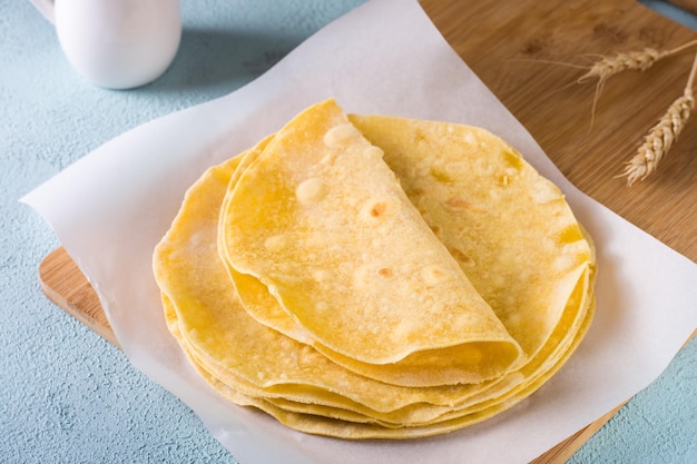 Stack of flat mexican corn tortillas on wooden board on table