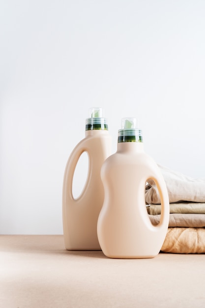 Photo stack of folded clean clothes things with eco design, blank bottles packaging of detergent for laundry