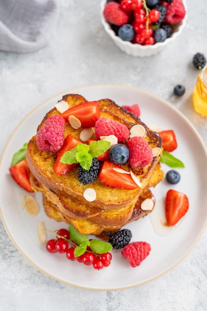 A stack of French toast on a plate with fresh berries, almond petals and honey on a gray concrete background. Delicious breakfast. Copy space.