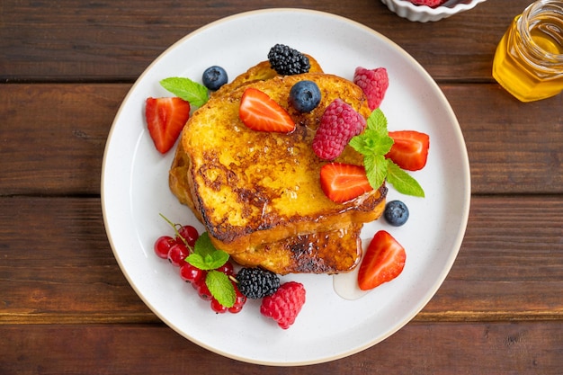 A stack of French toast on a plate with fresh berries almond petals and honey