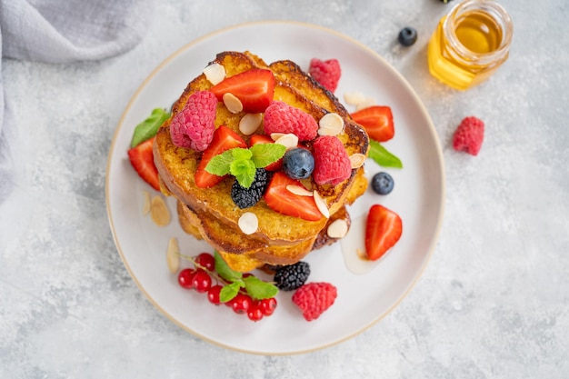 A stack of French toast on a plate with fresh berries almond petals and honey