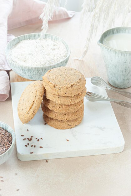 A stack of gluten free oatmeal cookies on a marble board with a bowl of milk in the background.