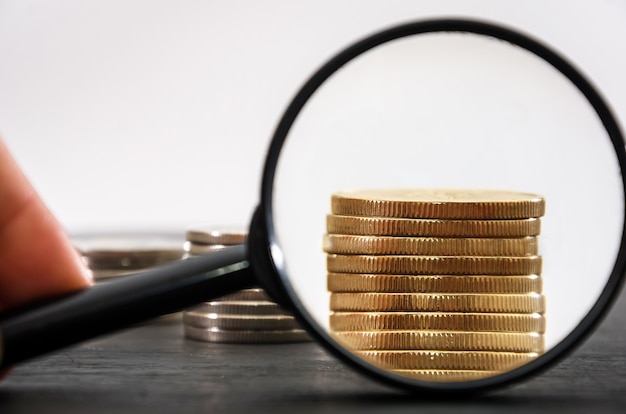 A stack of gold coins are visible through a magnifying glass