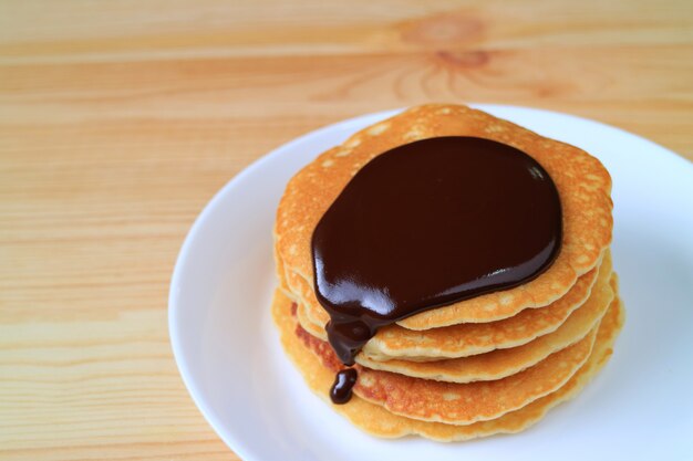 Stack of Home-made Pancakes with Hot Belgian Chocolate Sauce Served on Wooden Table