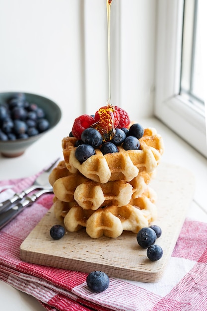 Stack of homemade waffles with raspberries and blueberries sprinkled with syrup