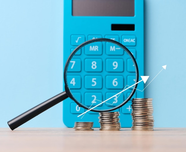 A stack of metal coins and a plastic magnifier on a blue background The concept of increasing taxes subsidies