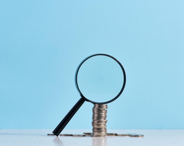 A stack of metal coins and a plastic magnifier on a blue background The concept of increasing taxes subsidies