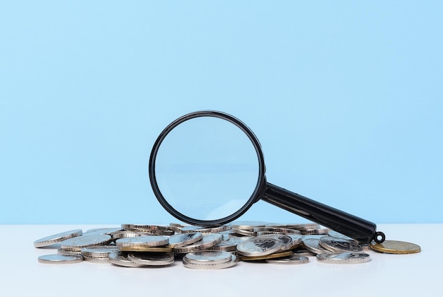 A stack of metal coins and a plastic magnifier on a blue background The concept of increasing taxes subsidies