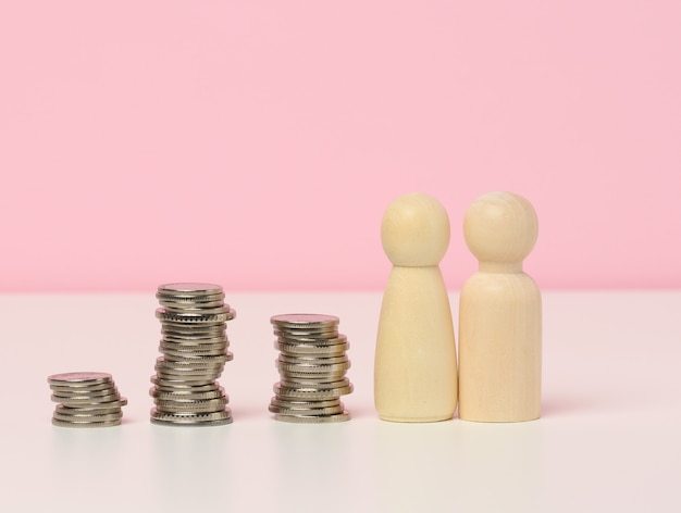 Photo a stack of metal coins and wooden figures of men on a white table. savings and expenses, family budget, subsidies from the state