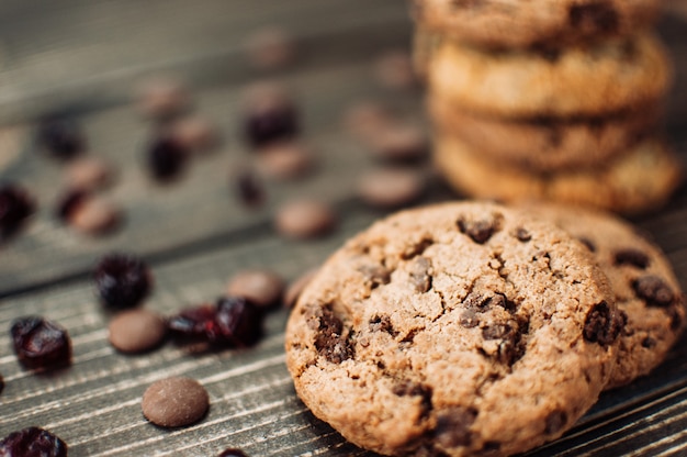 A stack of oatmeal cookies with chocolate pieces and candied fruits lies on a wooden table