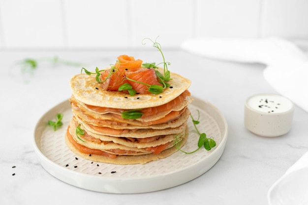 Stack of oatmeal pancakes with salted salmon and herbs closeup