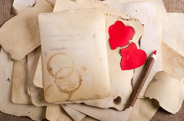 Stack old papers, notebook, wooden pencil and two vintage red hearts on burlap, sackcloth.