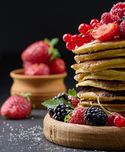 A stack of pancakes with fresh fruits poured with syrup on a black background