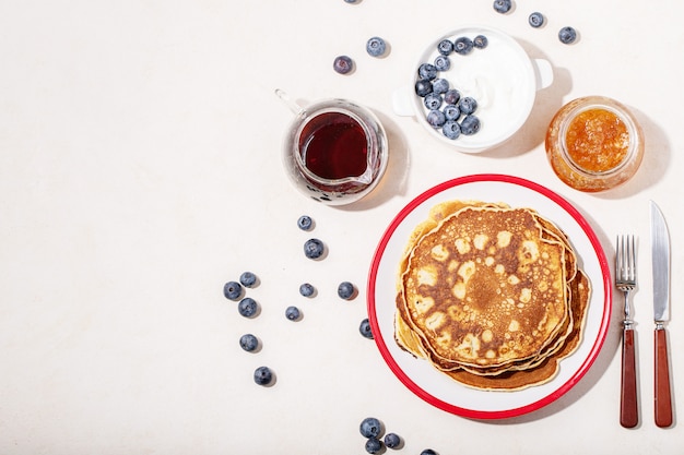 Stack of plain pancakes served with honey and blueberries