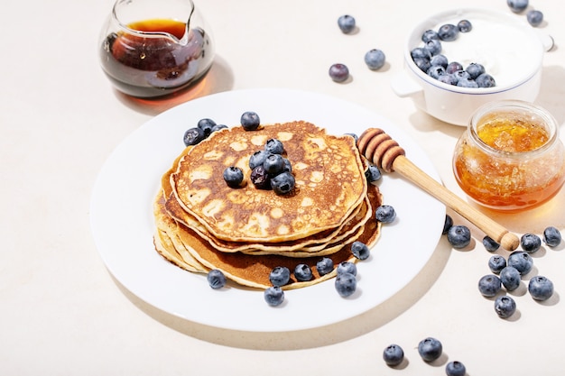 Stack of plain pancakes served with honey and blueberries