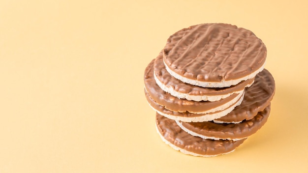 Stack of round rice cakes covered with dark chocolate on yellow background. Healthy Gluten Free cereal crispbread.