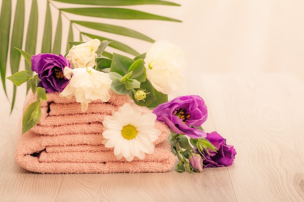 Stack of soft terry towels with white and violet flowers and green leaves on pink background