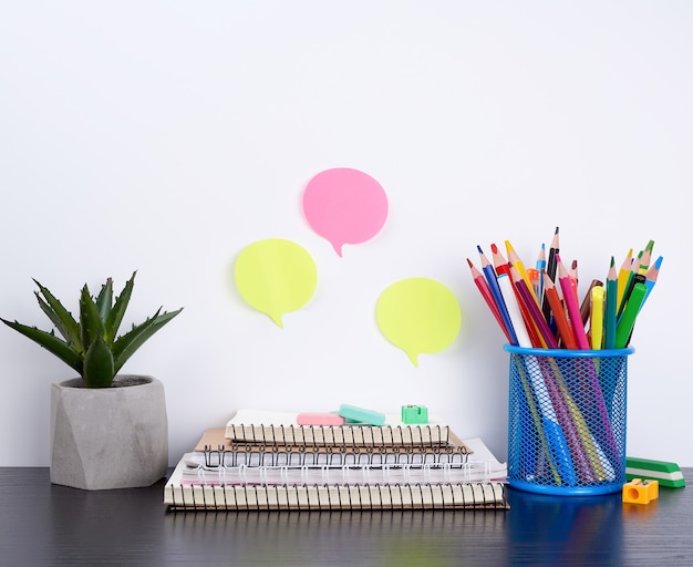 Stack of spiral notebooks and colored stickers, next to a ceramic pot with a flower