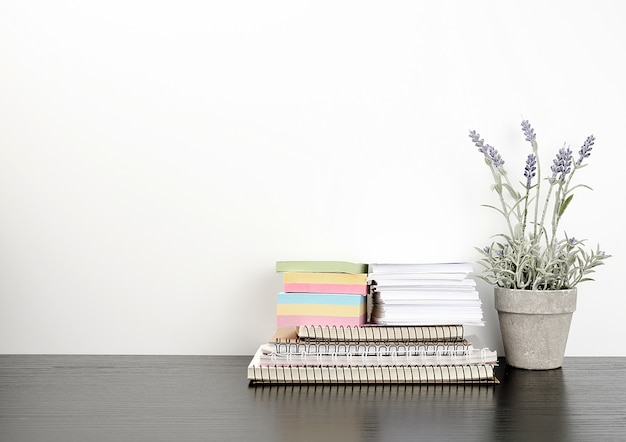 A stack of spiral notebooks and colored stickers, next to a ceramic pot 