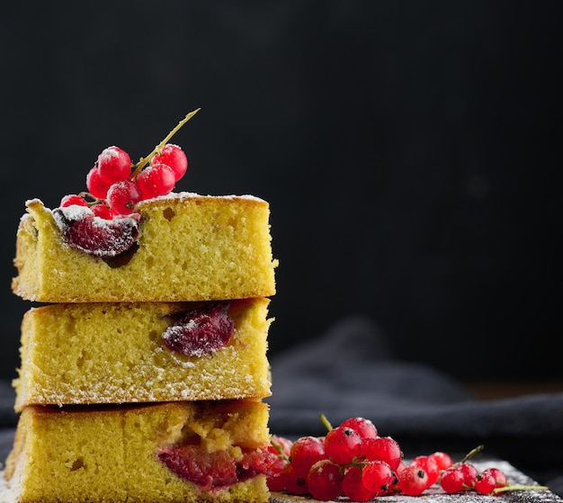 A stack of square slices of baked plum biscuit cake sprinkled with powdered sugar on top