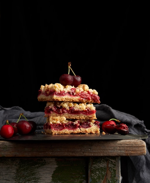 Stack of square slices of a pie with red cherry, black background