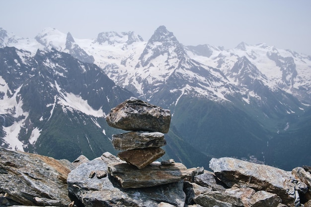 Stack of stones on top of the mountain against a background of mountain snow peaks