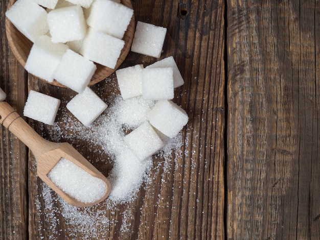 Stack of sugar cubes and granulated sugar in a wooden scoop