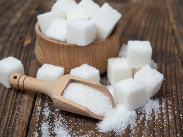 Stack of sugar cubes and granulated sugar in a wooden scoop