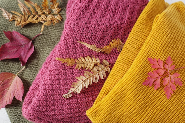 Stack of sweaters with autumn leaves on  white wooden table