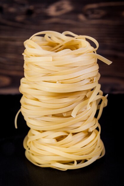 Stack of tagliatelle pasta nests over a dark wooden table