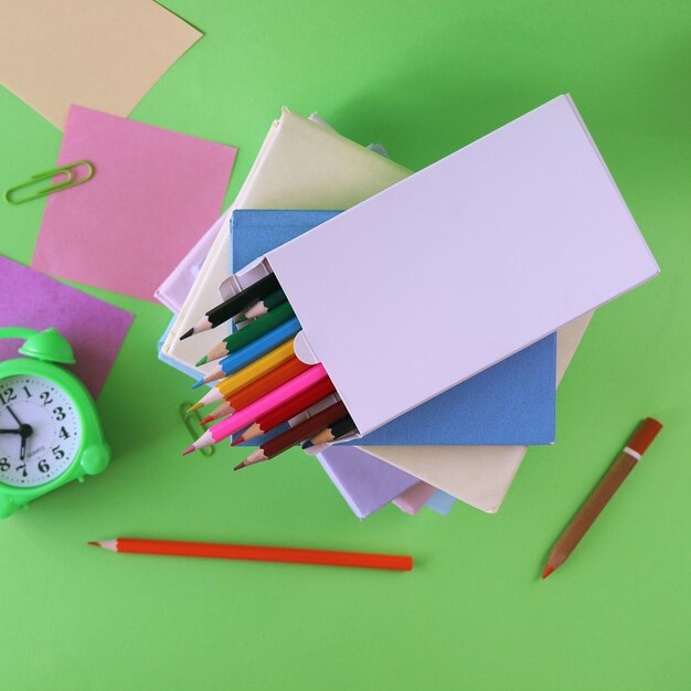 Stack of textbooks, alarm clock, apple and school supplies, green background