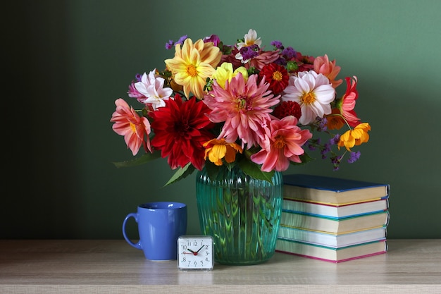 Stack of textbooks, a bouquet of dahlias and an alarm clock on the table. back to school.