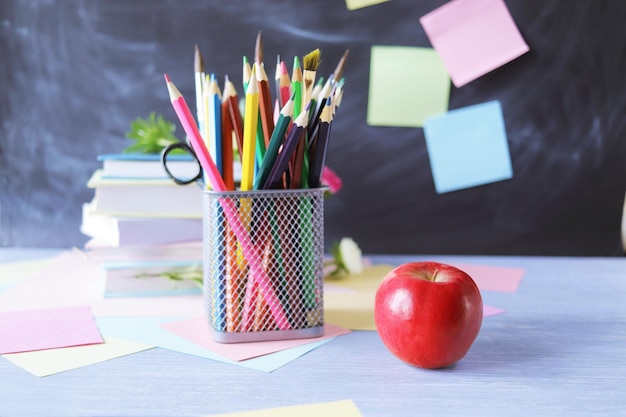 A stack of textbooks, multi-colored pencils, a red apple, on the background of a school board