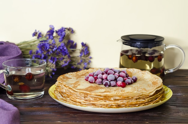 Stack of thin pancake with cranberries and icing sugar, drinks with rose hips on wooden table. soft focus. national Russian holiday, tradition, Shrovetide