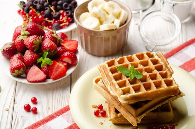 Stack of three belgian waffles on white kitchen table with strawberries bananas and red currant