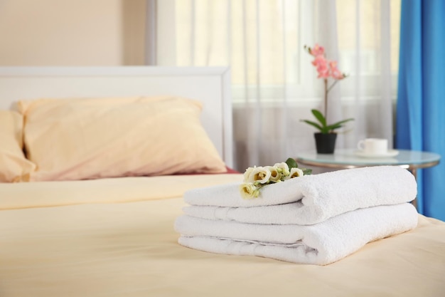 Stack of towels and flowers on bed in hotel room