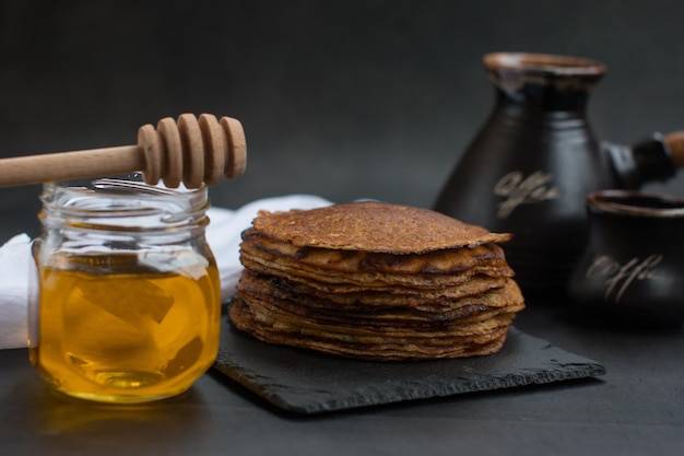 Stack of traditional Russian pancakes with honey on black background with Homemade Russian thin pancakes Russian national cuisine