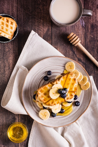 A stack of waffles with banana blueberries and honey on a plate Comfort food Top and vertical